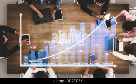 A business team collaborates during a meeting, analyzing digital graphs on laptops and tablets, discussing strategies for growth and performance impro Stock Photo