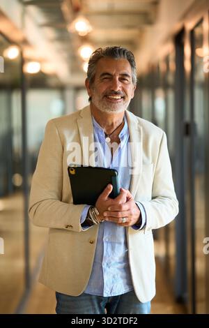 Mature businessman smiling and holding a tablet in office Stock Photo