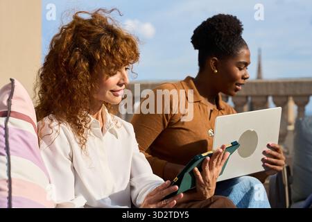 Diverse women collaborating on technology device outdoors Stock Photo