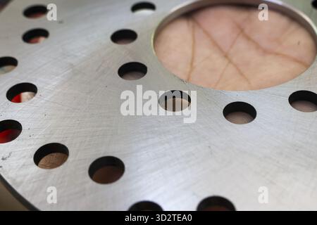 Detailed close up of metal disc brake surface with ventilation holes. An industrial and mechanical automotive part with hand visible through large ope Stock Photo