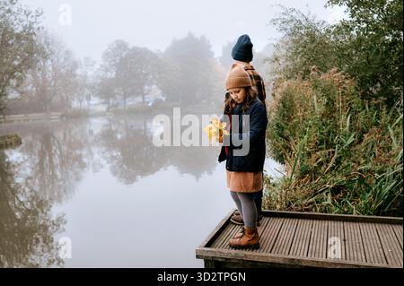 Kids standing on pier holding autumn leaves in hands. Stock Photo