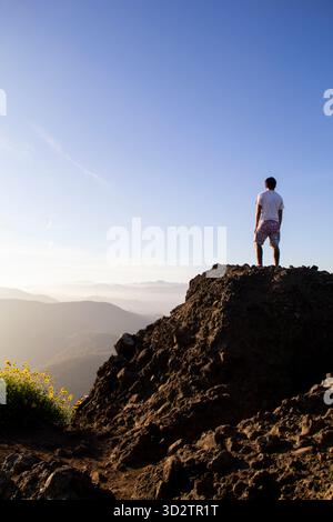 Man standing on rocky summit looking out over misty mountain valley Stock Photo
