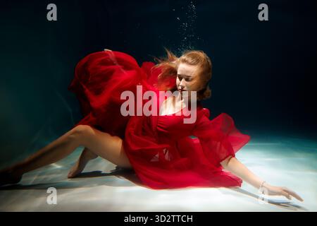 Woman in red dress gracefully swimming in crystal clear water Stock Photo