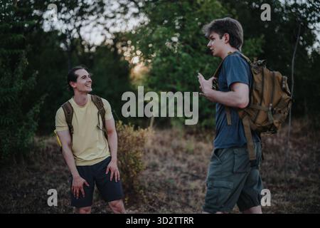 Two friends hiking and talking on a forest trail with backpacks and casual outdoor gear Stock Photo