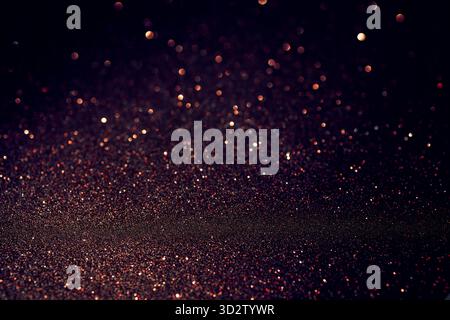 Dark glitter surface glowing with warm copper sparkles, lower frame textured in focus while upper area melts into soft blur filled with luminous bokeh Stock Photo