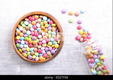 Candy coated chocolate lentils, in a wooden bowl, on linen. Small, sugar-coated chocolate dragees, with multi colored candy shell. Stock Photo