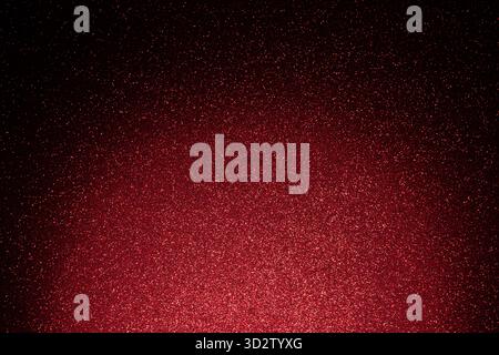Dark red glitter texture with full surface focus, luminous spot below fades upward into shadow while countless sparkles shimmer across granular relief Stock Photo