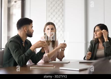 Three professionals engaged in brainstorming session, focused conversation at table Stock Photo