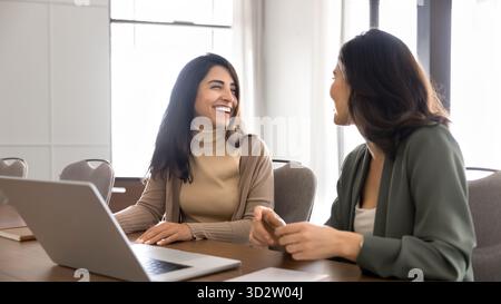 Two happy professional women sitting at meeting table with laptop Stock Photo