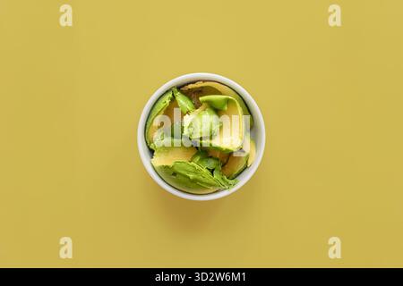 Top view fresh ripe avocado slices in white ceramic bowl on vibrant yellow background. Healthy vegan food for diet, guacamole and salad ingredient Stock Photo
