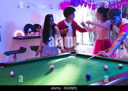 Teenagers playing pool and celebrating birthday in colorful party room. Celebration, billiards, fun, friends, joyful, leisure || Model released Stock Photo