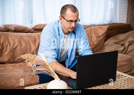 Handsome young man sitting on the couch and working on laptop computer, working remotely from home. Social distancing Self Isolation || Model released Stock Photo