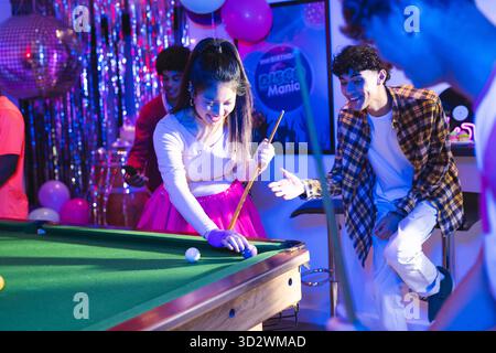 Teenagers playing pool at party, enjoying vibrant celebration with friends. Billiards, socializing, entertainment, leisure, fun, recreation || Model released Stock Photo