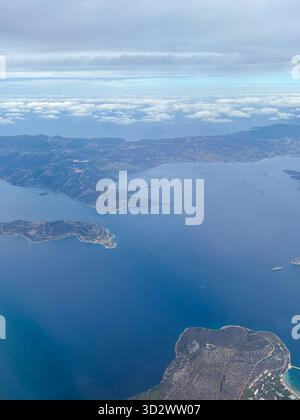 Stunning aerial shot of small islands scattered in a tranquil blue sea with distant mountains and soft cloud cover. Stock Photo