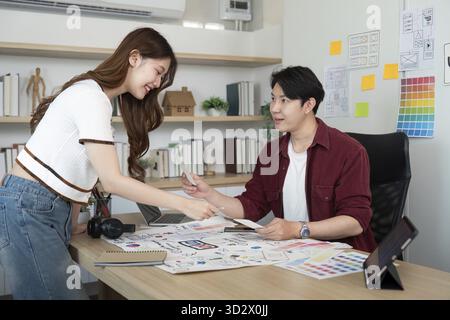 A young woman and man engage in a discussion over UX UI design concepts, showcasing teamwork in a modern office Stock Photo