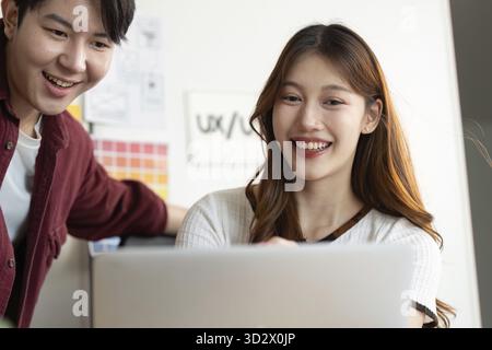 Two young professionals sharing a moment of joy while collaborating on a UX design project on a laptop Stock Photo