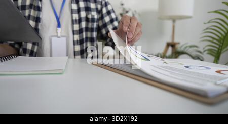 A young Asian man reviewing documents on a tablet while seated at a modern home office desk, promoting a healthy work-life balance in a vibrant enviro Stock Photo