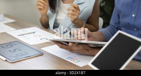 Two professionals collaborating in an office setting, analyzing ESG strategies on a tablet and papers, reflecting teamwork and sustainability efforts Stock Photo