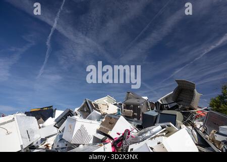 A vast heap of discarded appliances, furniture, and metal clutter lies in an open junkyard against a bright sky. The chaotic pile highlights waste, re Stock Photo
