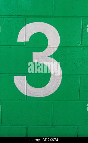 A white painted number 3 on a green brick wall Stock Photo