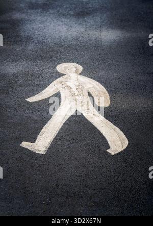 A white painted symbol of a man walking on a tarmac road, indicates the way pedestrians should walk Stock Photo