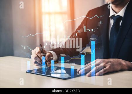 A businessman is analyzing financial data on a digital tablet, surrounded by graphs and charts that represent market growth, in a contemporary office Stock Photo