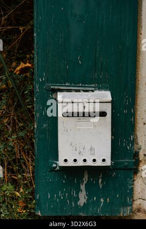 Weathered white mailbox mounted on an aged dark green wooden door with peeling paint. A charming, rustic detail capturing the character of an old Euro Stock Photo