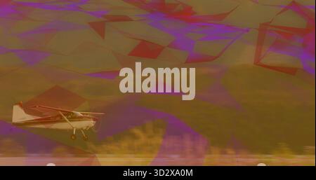 Flying small single-engine propeller airplane skimming grassy field, with landing gear and hillside Stock Photo