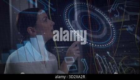Technician wearing white shirt monitoring holographic interface in server room, with network cables Stock Photo