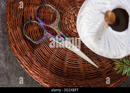 Close-up of colorful embroidery scissors and a crochet hook in a spool of white cotton thread on a dark stone background. Handicraft, crochet, and DIY Stock Photo