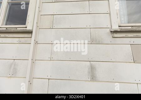 Some old and worn white asbest tiles on an outer house wall. Asbest wall tiles were popular in older days. Many houses still have these health threath Stock Photo