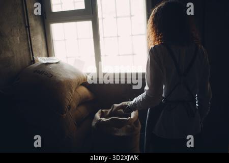 Green coffee beans in burlap sack and woman roaster with scoop Stock Photo
