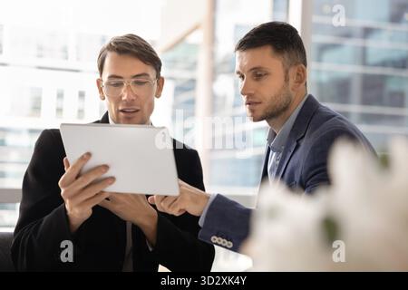Two busy young male business coworkers using tablet for teamwork Stock Photo