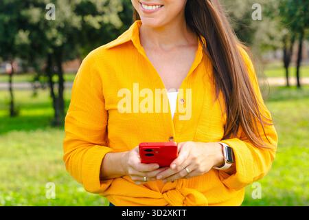 Smiling woman lying on grass outdoors using smartphone and looking down Stock Photo
