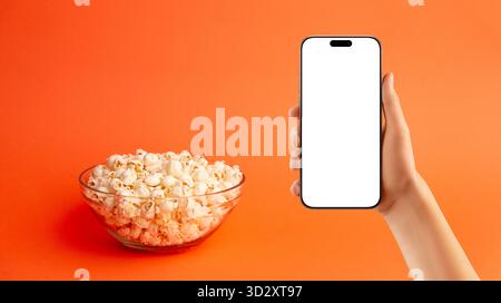 Minimalist flat lay of popcorn bowl surrounded by scattered kernels on orange background, ideal for snack, design, and creative food visuals Stock Photo