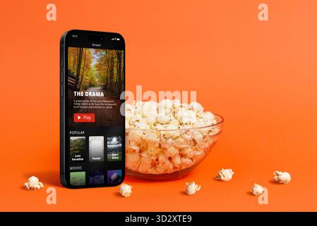 Cinematic concept with popcorn falling into a glass bowl on an orange background, symbolizing fun, snacks, and movie entertainment in a minimalist stu Stock Photo