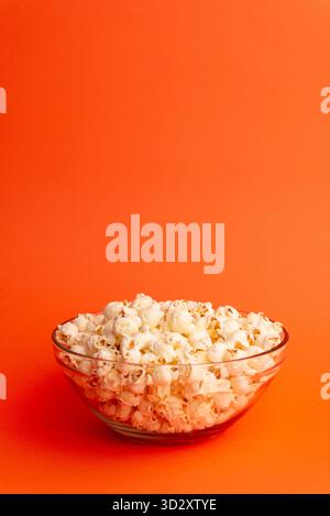 Studio photo of popcorn falling above a transparent bowl on orange background, combining motion, food concept, and minimalist cinematic design Stock Photo