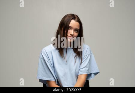 Smiling young woman with gentle expression posing in light blue t-shirt Stock Photo