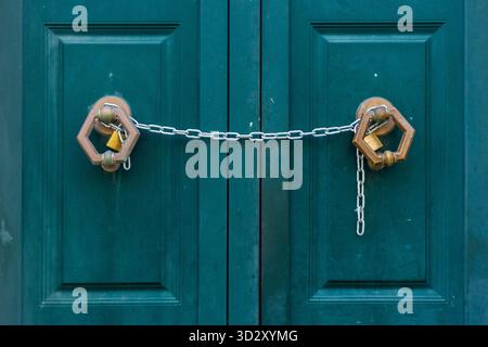 Teal Double Doors Secured With Chains And Padlocks Across Panels Of A Metal Gate Stock Photo