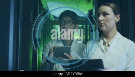 Two IT technicians projecting and analyzing 3D interface in hall, with server racks and tablets Stock Photo