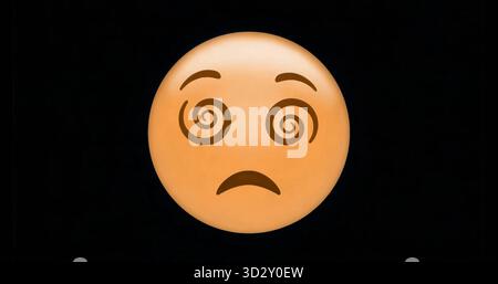 Displaying yellow-orange emoji face with spiraling eyes on black background, expressing confusion Stock Photo