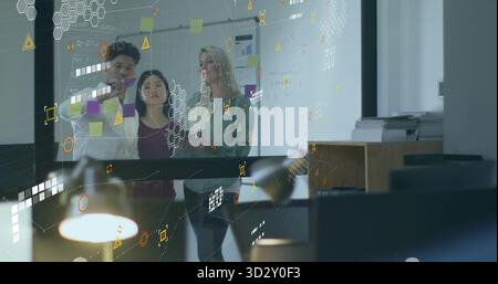 Three professionals writing on glass planning wall in office, with colleagues reviewing notes Stock Photo