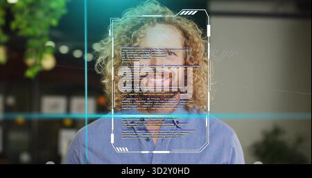 Standing man with curly red hair smiling in office, with code UI overlay and lapel mic Stock Photo