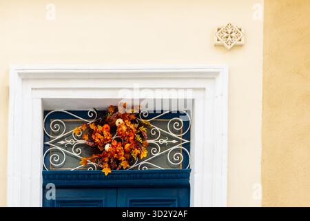 Autumn Wreath Adorns Blue Door With White Ornate Grille On Sunlit Wall Stock Photo
