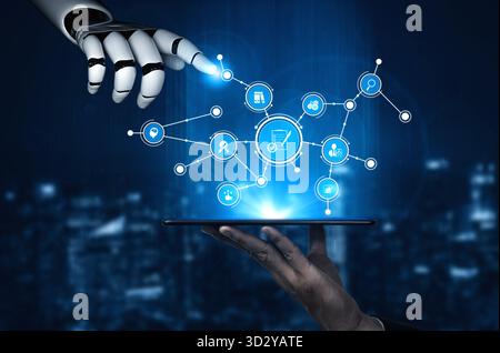 A sleek robot hand interacts with floating digital icons above a tablet screen, illustrating advanced technology and automation in a modern urban sett Stock Photo