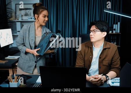 Serious face of working sales manager with secretary taking overworked folder paper at over late night checking collected signing document for board c Stock Photo