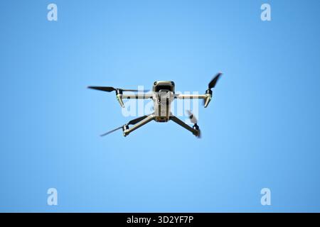 A drone is flying in the sky. The sky is blue and clear. The drone is in the air and is not touching the ground Stock Photo