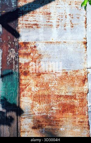 Sheet-metal shed roof with strong texture, partly rusty and partly painted green, sunlit and captured in warm analog tones. Stock Photo