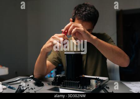 Portrait of serious focused computer technician installing CPU cooler onto motherboard with screwdriver, conducting maintenance and upgrades on Stock Photo