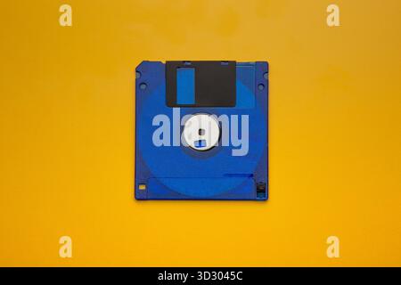 Vibrant blue 3.5-inch floppy disk centered on a bright yellow, contrasting background. Stock Photo